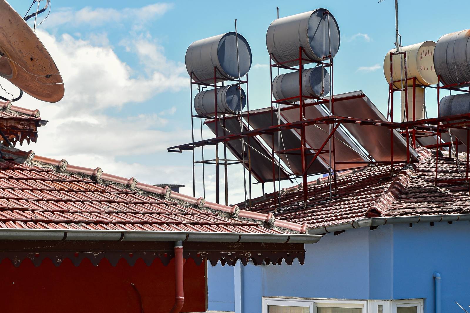 Solar water heaters and storage tanks mounted on steel frames above a tiled roof