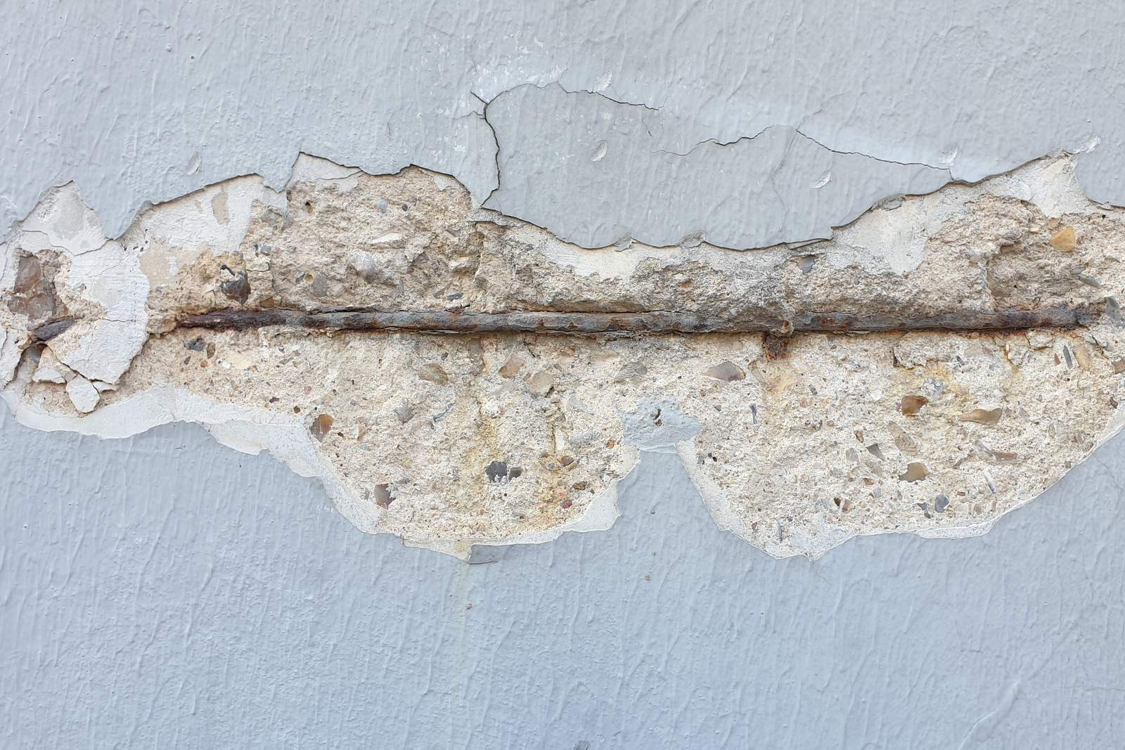 A long horizontal crack in a rendered wall, broken open to show the corroded reinforcement bar running through it