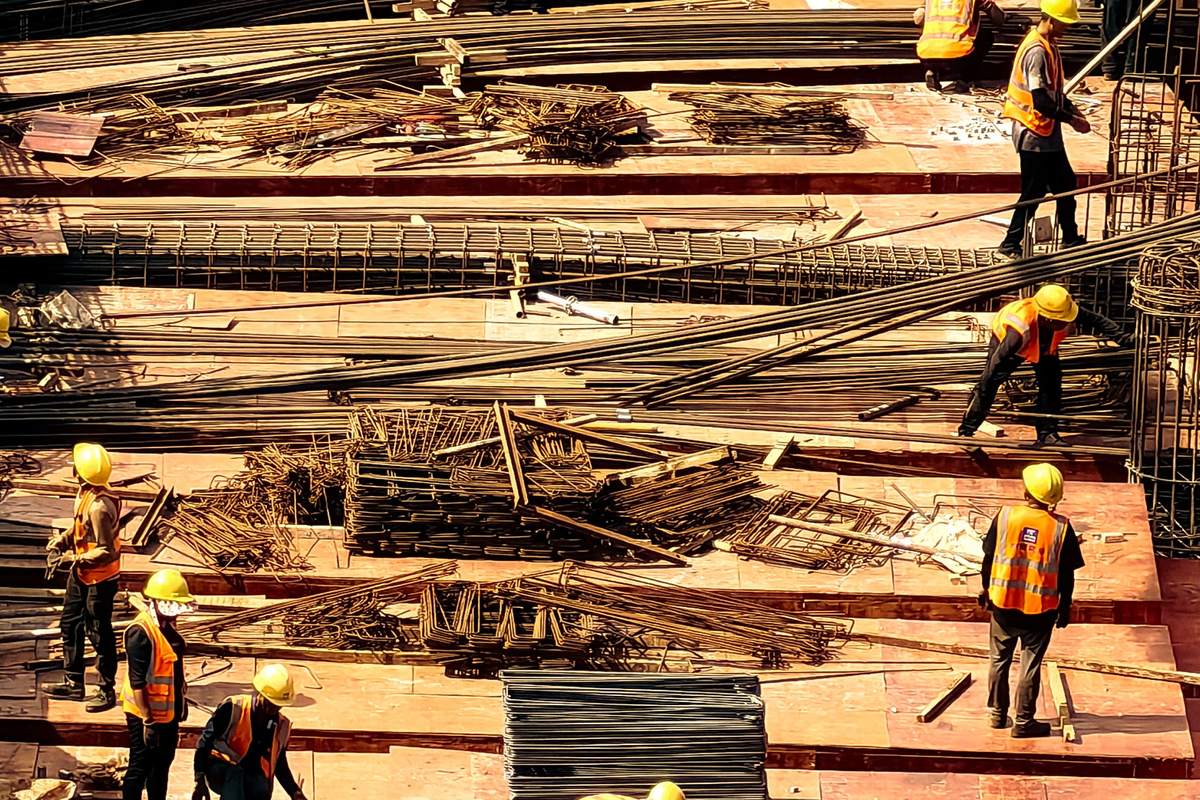 Workers on a raised concrete deck, laying and tying reinforcement bars across the slab before a pour