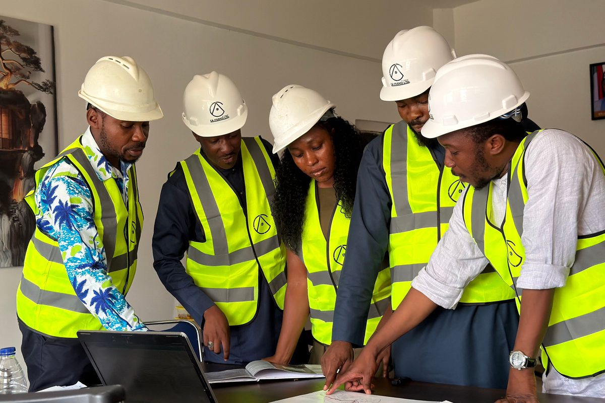 Five people in hard hats and marked hi-vis vests standing around a boardroom table, working through a drawing and a laptop together
