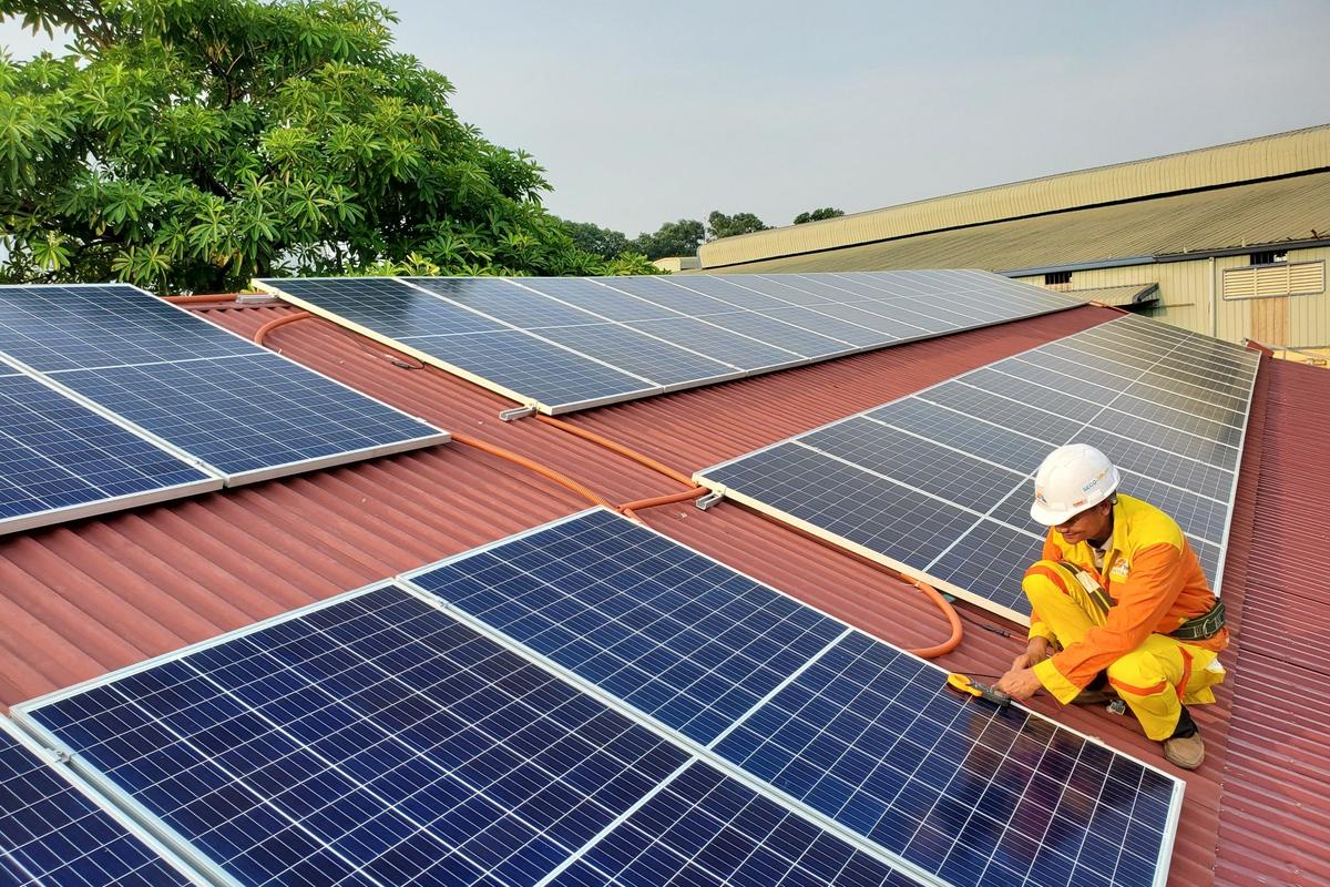 A technician in overalls kneeling to fit solar panels across a corrugated metal roof