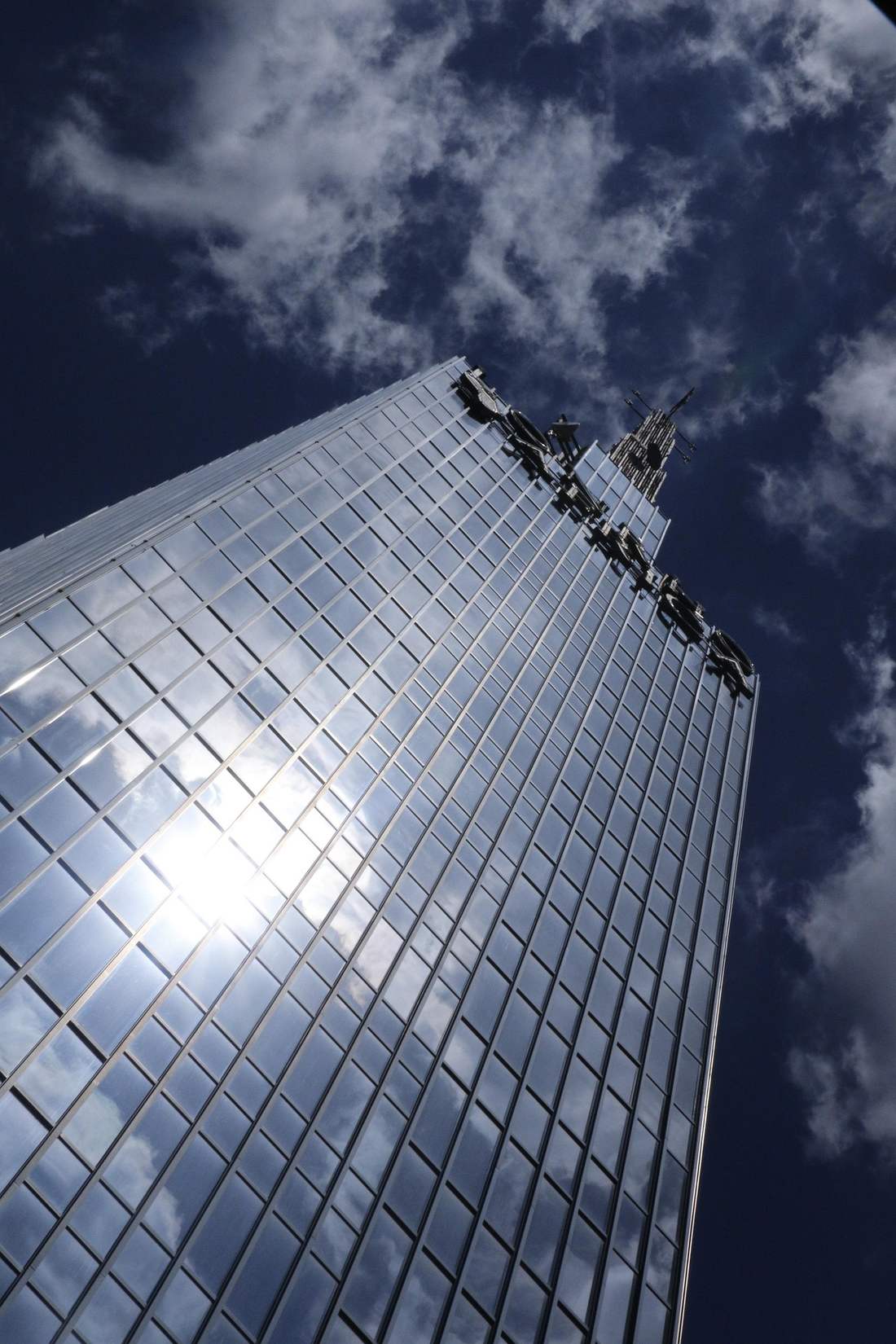 A glass office tower seen from street level against a bright sky